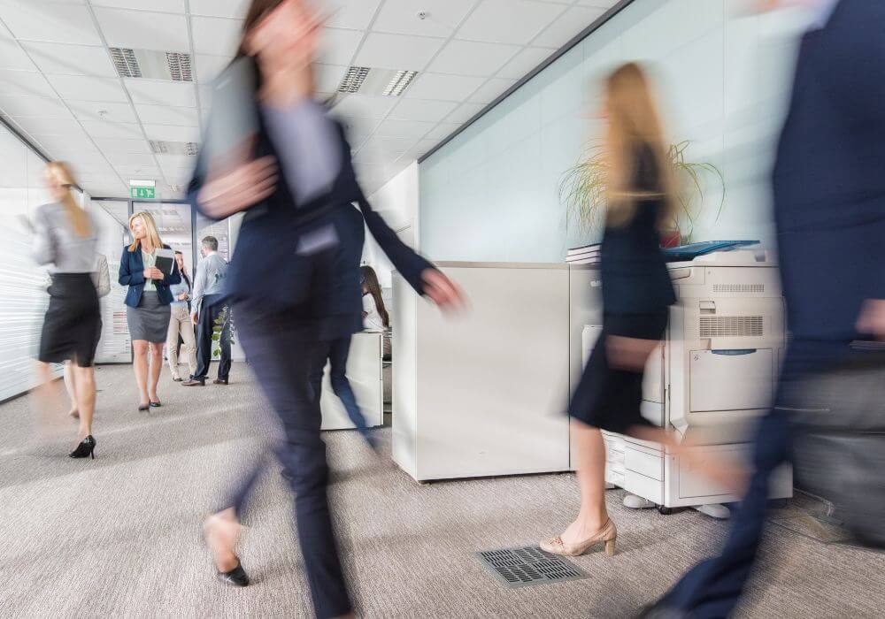 Blurred figures walking through a busy office environment, representing article on recruiter risks and how insurance can help