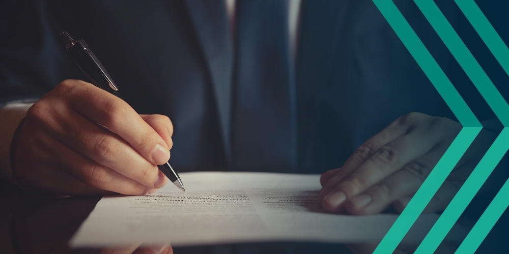 Close-up low-angled photo of person hovering a pen over a contract, representing article on recruiter contract risks and clauses to look out for