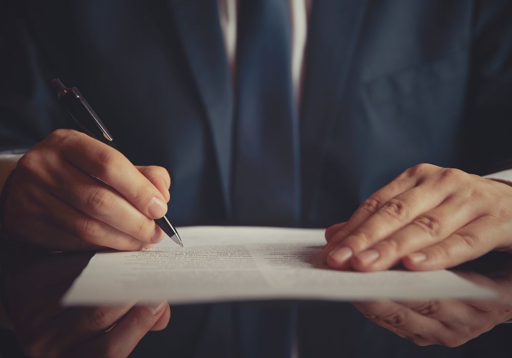 Close-up low-angled photo of person hovering a pen over a contract, representing article on recruiter contract risks and clauses to look out for